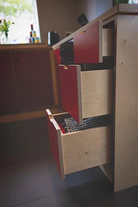 Red-fronted plywood kitchen drawers opened to show fitted storage