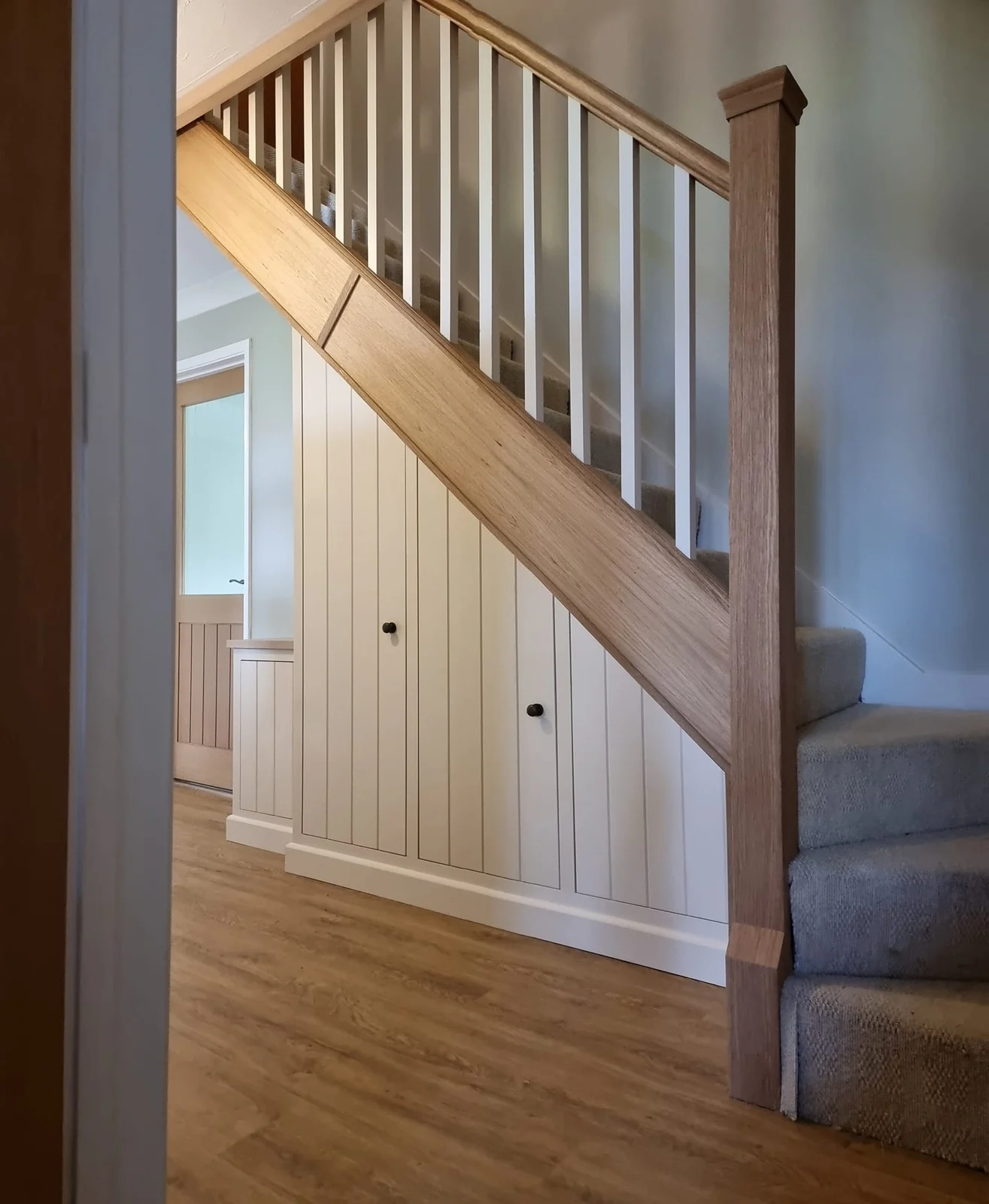 White panelled understair storage and natural wood staircase